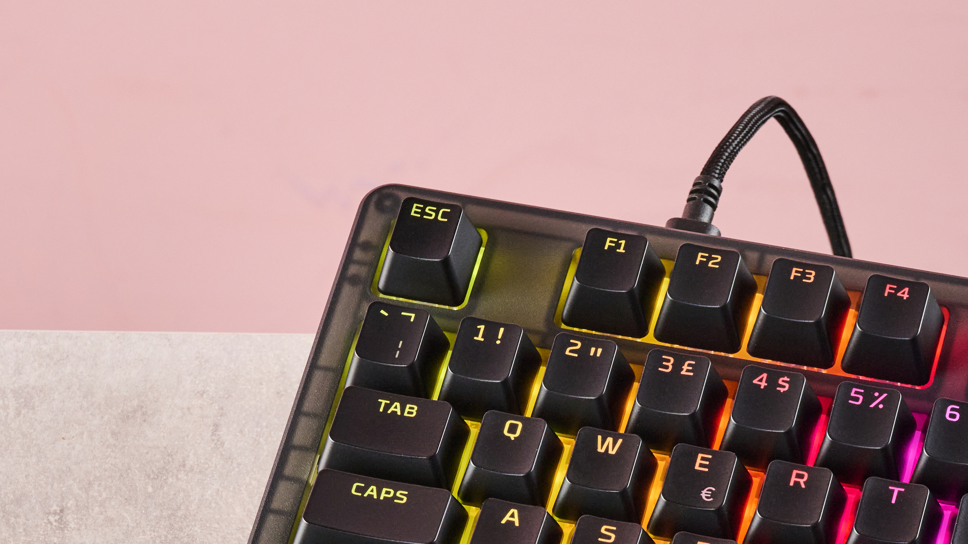 Close-up of top-left corner of HyperX Origins 2 1800, with RGB backlighting on, on a desk with pink wall in background