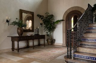 entry foyer with pale stone floors and staircase with tiled risers and cast iron spindles and dark wood console with white walls