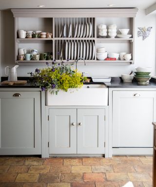 Pale blue shaker style kitchen cupboards with Belfast sink and plate rack above on wall