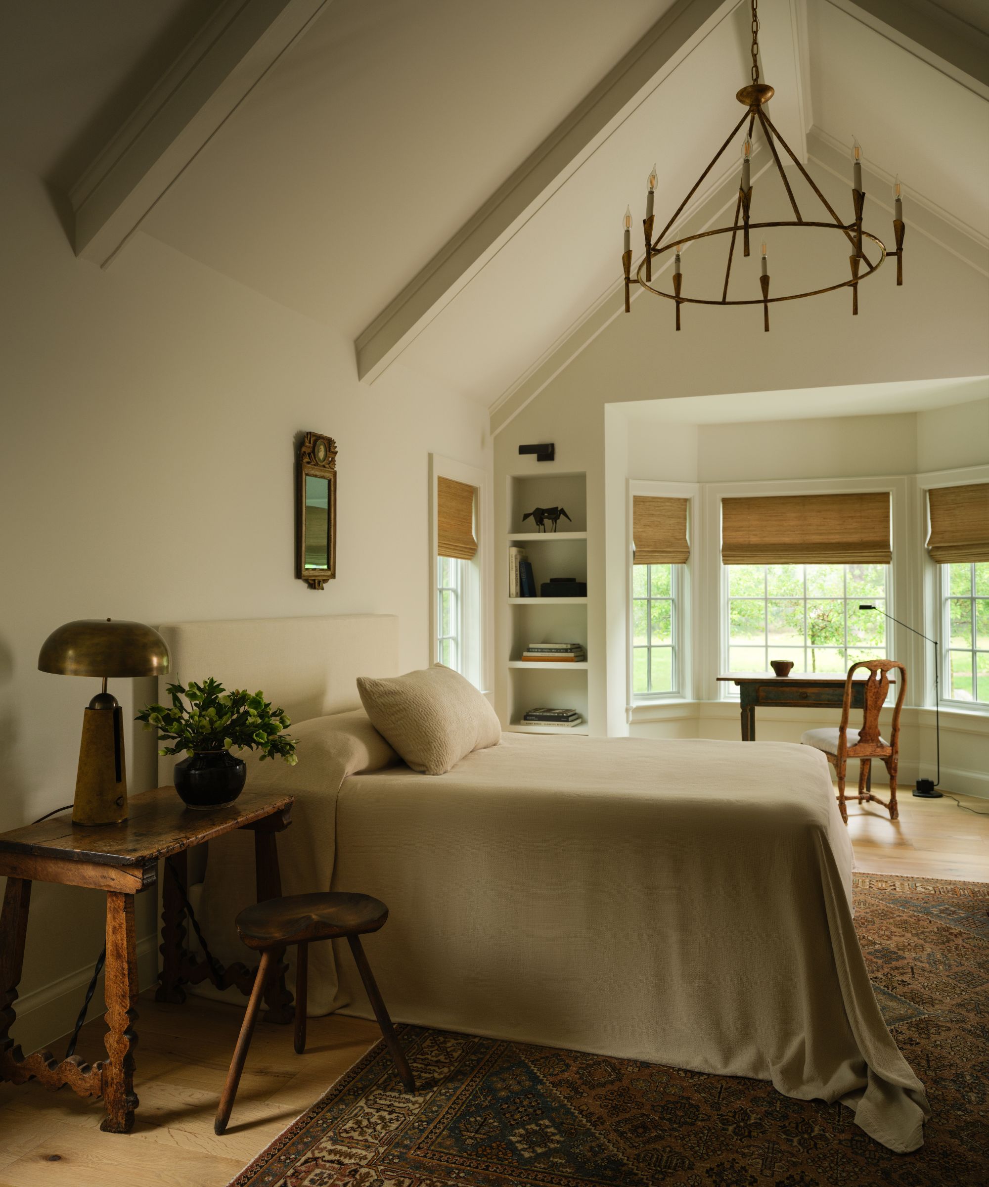 a neutral primary bedroom with vaulted ceiling, bay window alcove, vintage rug and furniture pieces