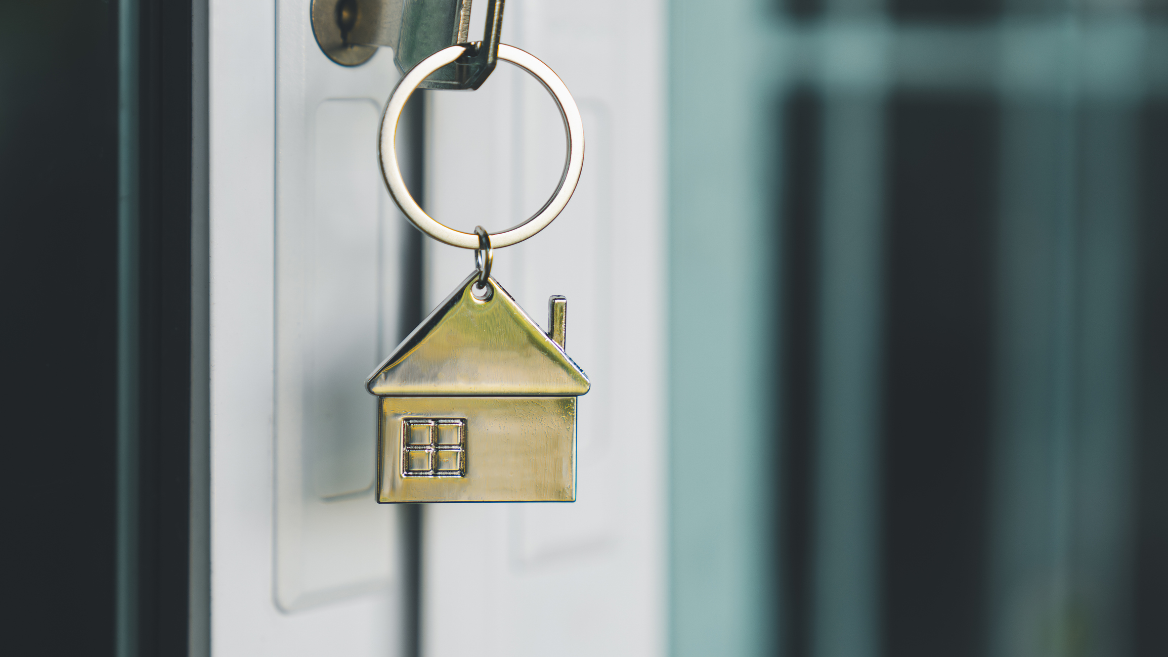 house shaped keychain in the lock of a model house front door