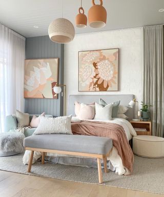 Layered lighting sources including bedside lamp, floor lamp, and mixed ceiling pendants trio, in pastel and neutral bedroom scheme, featuring floral artwork and pillows galore.
