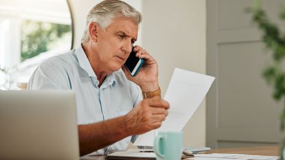 An older man looks at paperwork and talks on the phone at home.