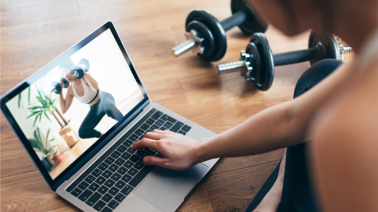 Woman looking at laptop screen with dumbbells on floor