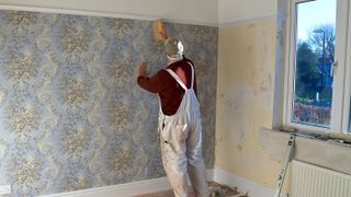 Man putting up patterned wallpaper near window