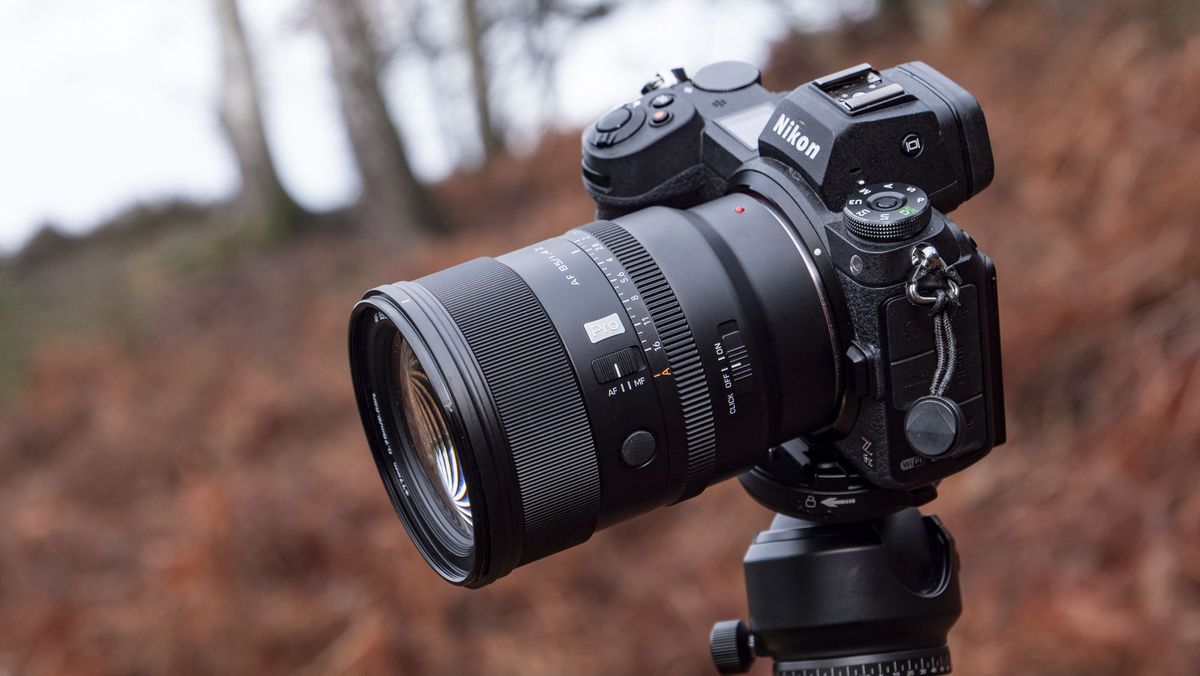 Viltrox AF 85mm F1.4 Pro lens attached to a Nikon camera, mounted to a tripod outdoors and with bronze-colored ferns in the background