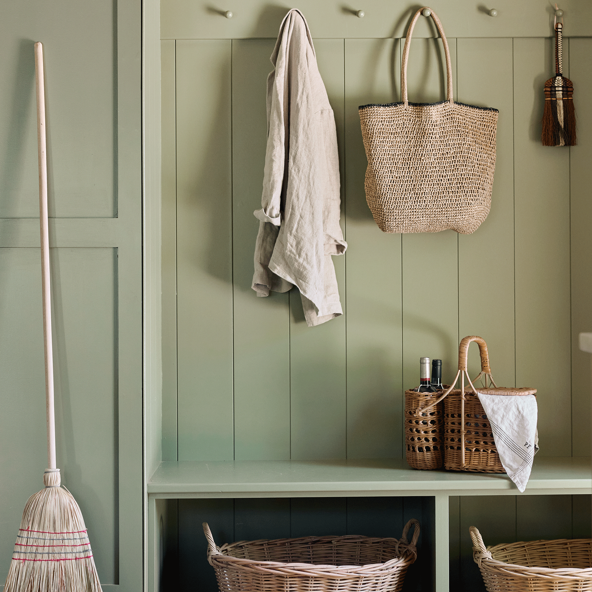 a green boot room area with peg rail, bench and baskets