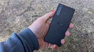 A black Sony Xperia 5 IV being held above and laid on a stony surface