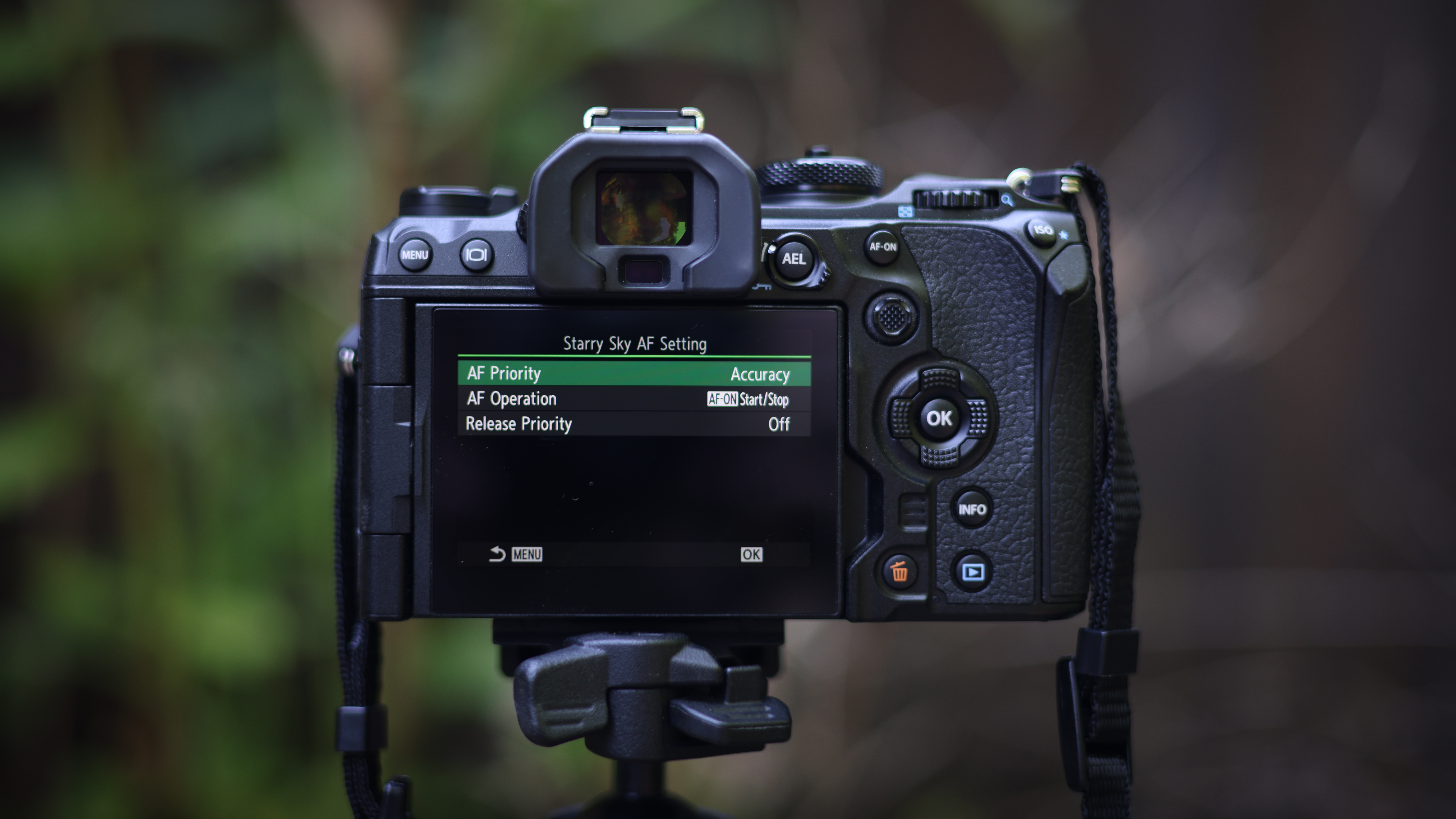 The OM System OM-1 camera body, against a woodland background