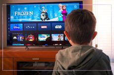 A boy looking at a TV showing the Disney+ home screen