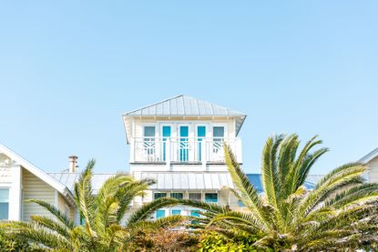 Image of a white house surrounded by palm trees and clear blue sky. 