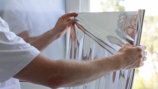 A man applying aluminum foil to a window