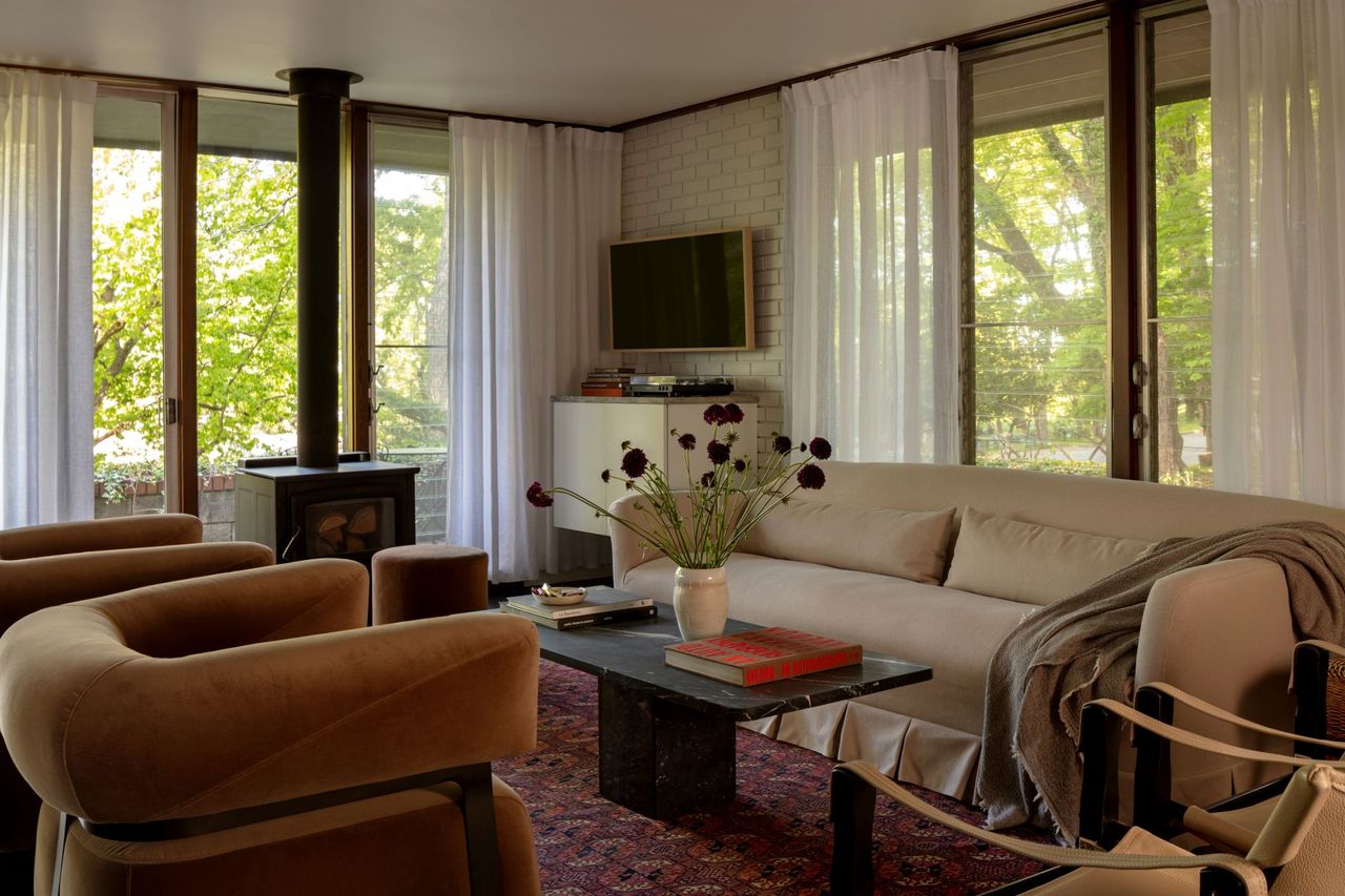 a living room with two brown accent chairs, a marble coffee table, a beige sofa, and a hang-down fireplace
