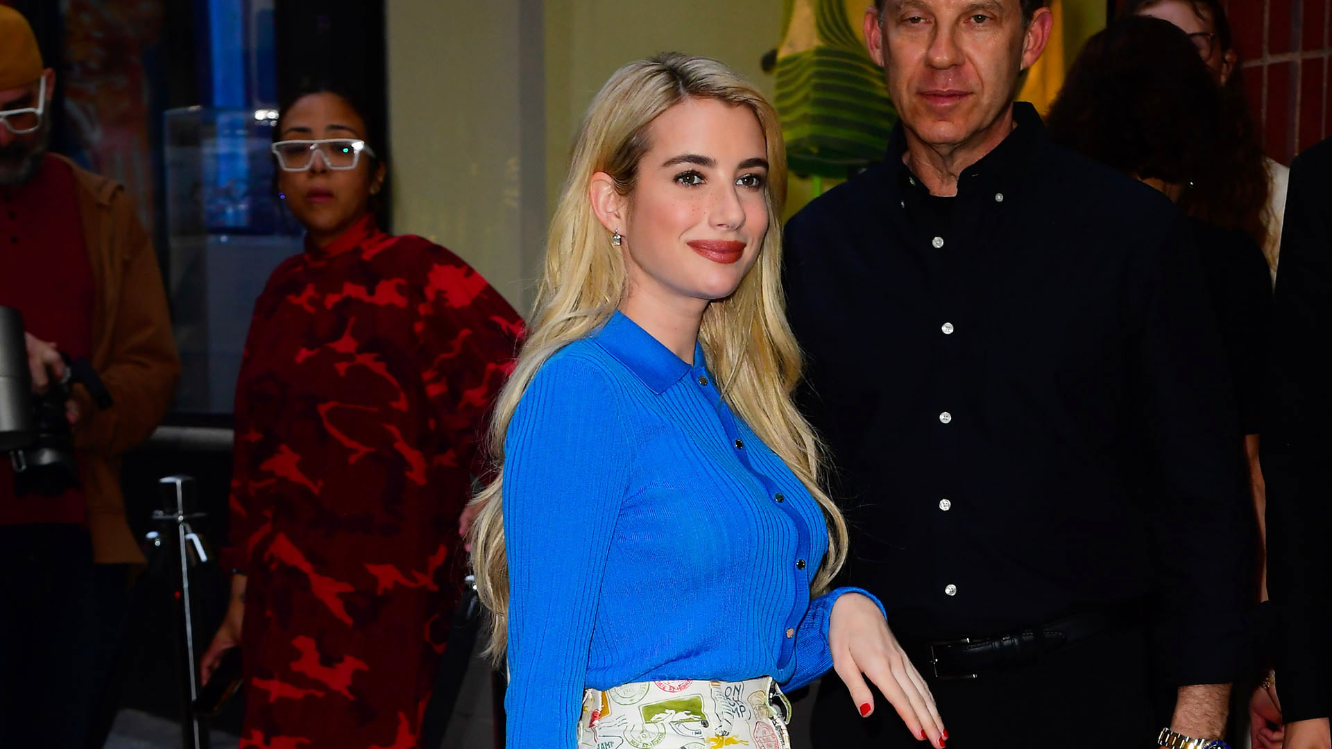 Emma Roberts wearing a blue cardigan, canvas print knee-length skirt, yellow handbag, and silver flats