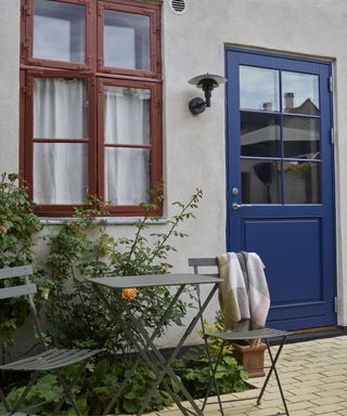 garden space with painted red window and blue back door with bistro table and chairs