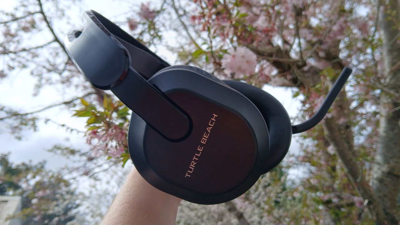 A Turtle Beach Stealth 500 headset in the black colourway, held up outdoors with a tree in the background.