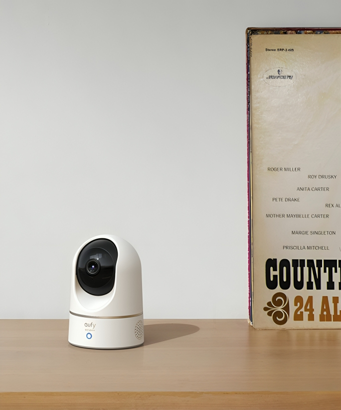 A eufy security camera on a wooden surface next to a vinyl record leaning against a wall