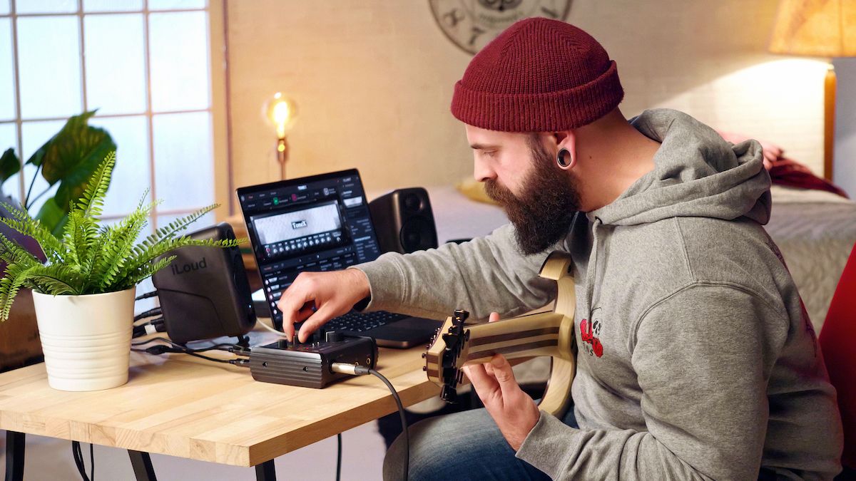 Man holding guitar adjusts settings on his audio interface