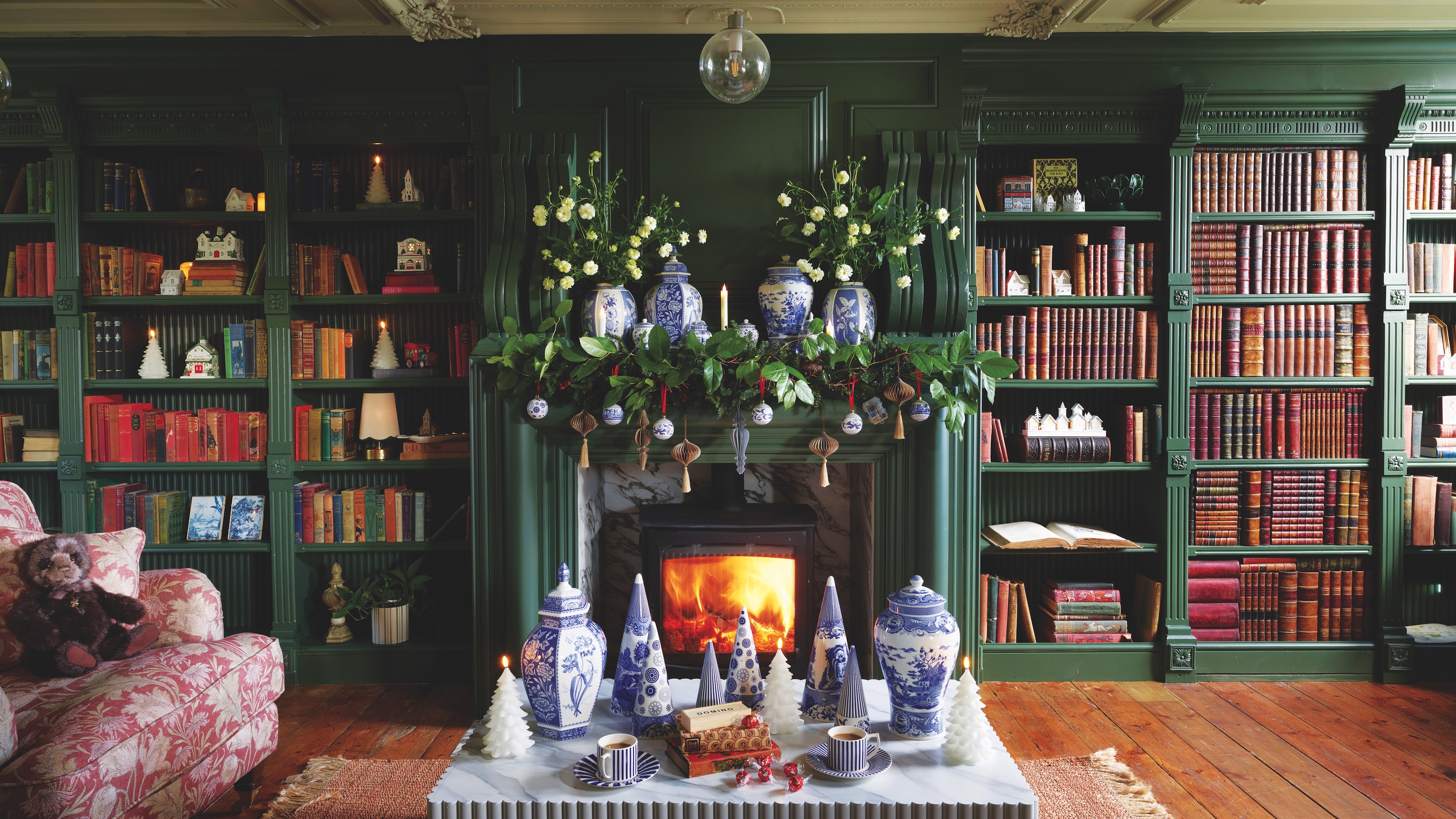 dark green library room with bookshelves around fireplace with woodburner and fluted marble-look coffee table
