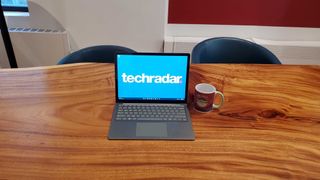 Bästa laptops för skrivande: En Microsoft Surface Laptop 4 står på ett bord på ett kontor bredvid en kaffemugg, med TechRadar-logon som bakgrundsbild.
