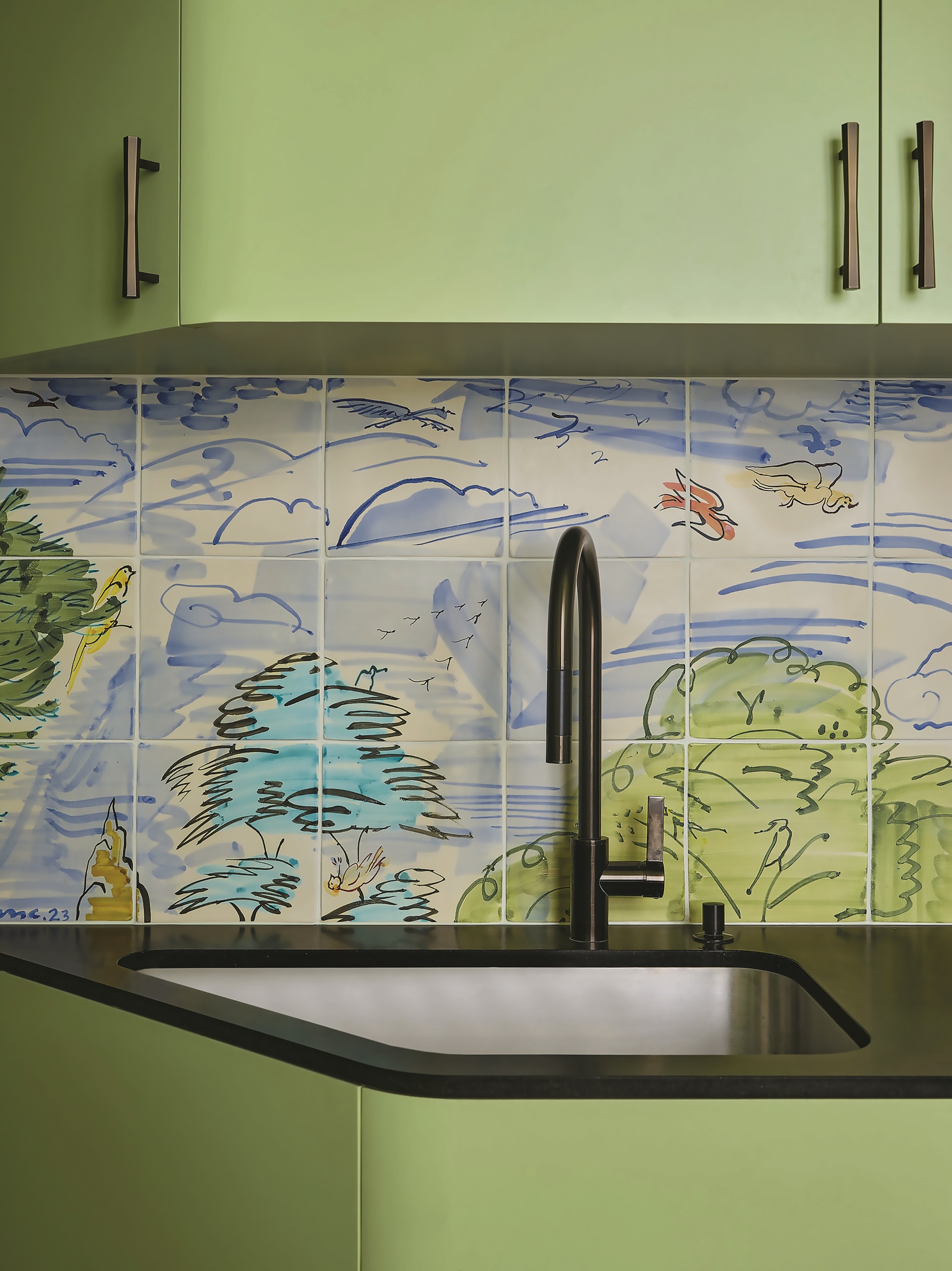 green kitchen with painted backsplash tiles, black counter with black tap