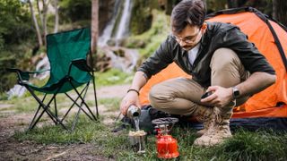 Man using camping stove to prepare pasta outside tent