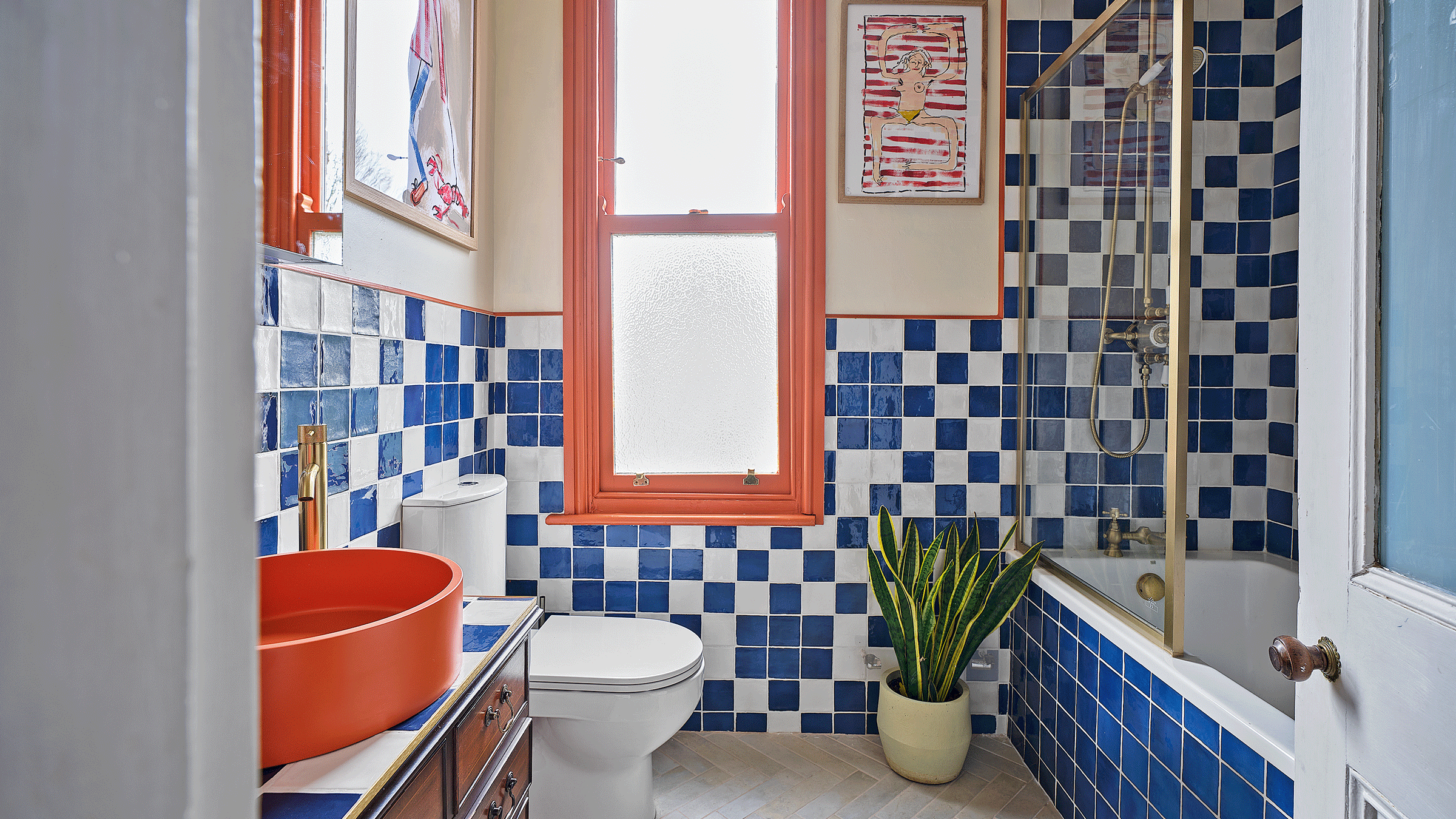 an orange and blue bathroom with blue and white checkered tiles with a shower bath and a glass screen and an orange basin