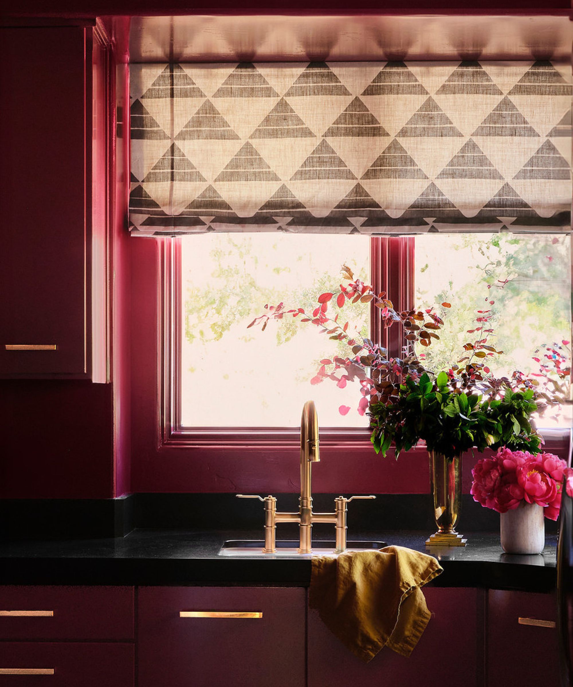 A laundry room color-drenched with a wine red paint, a window with a blind in a geometric print, and brass hardware.