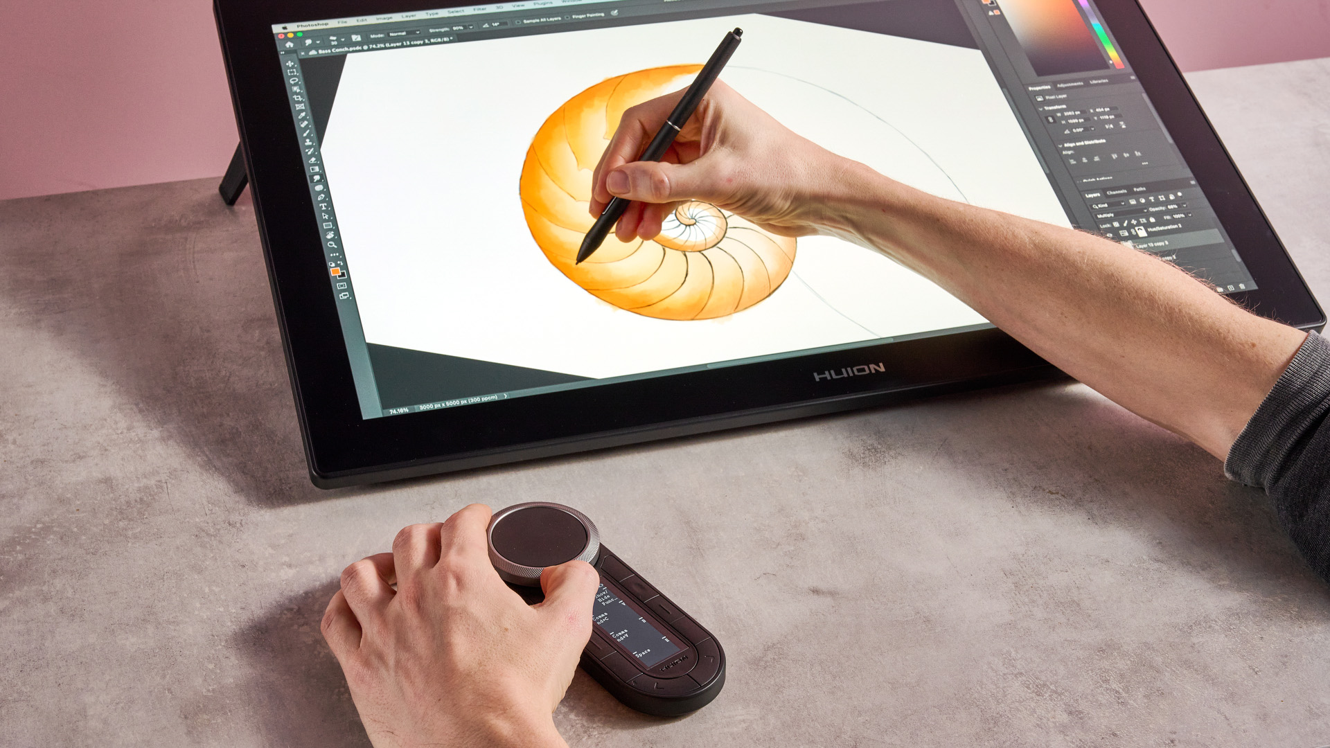 A hand paints with an orange oil brush on a sketch of a nautilus shell on the Huion Kamvas Pro 24 Gen 3, while another adjusts one of the twin dials of the Keydial Remote.