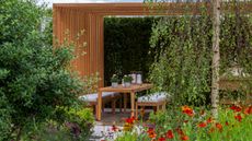pergola with outdoor seating area including table and garden benches, with silver birch tree, shrubs and orange helenium flowers