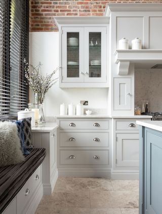 White kitchen with elements of blue and gray, an exposed brick and shaker style cabinetry. wall