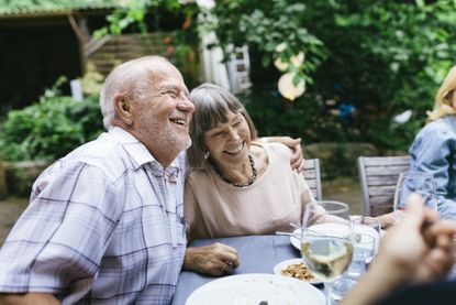 An elderly couple embracing, enjoying an outdoor meal with the family in a courtyard.
