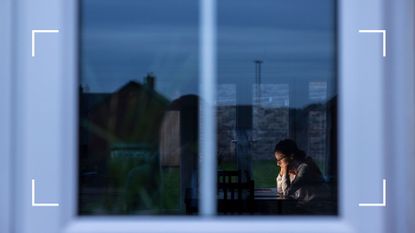 View of woman through an outside window sitting on laptop late at night
