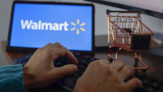 Man typing on a gaming keyboard with tablet showing Walmart logo next to a 1/6 scale shopping cart