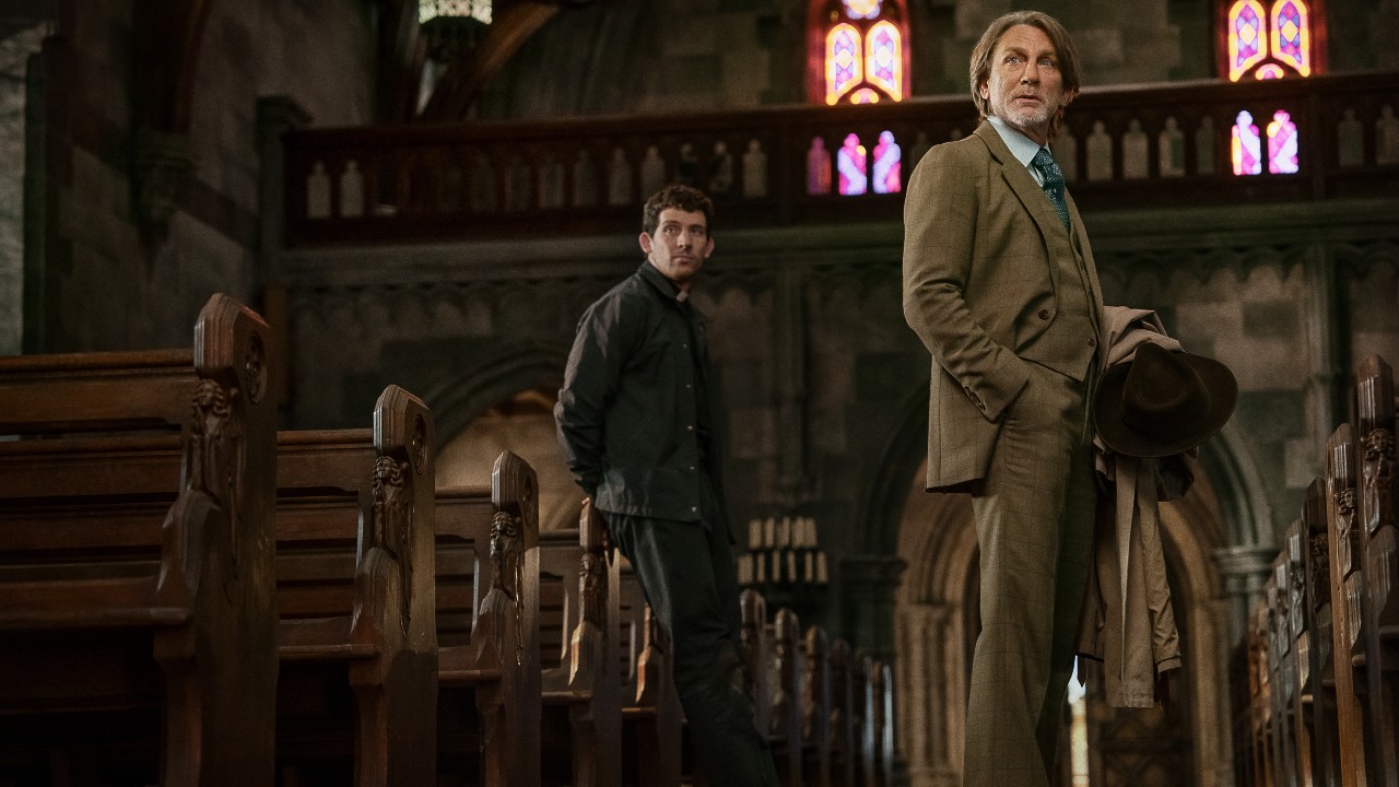 The priest and Benoit Blanc stand in the church aisle