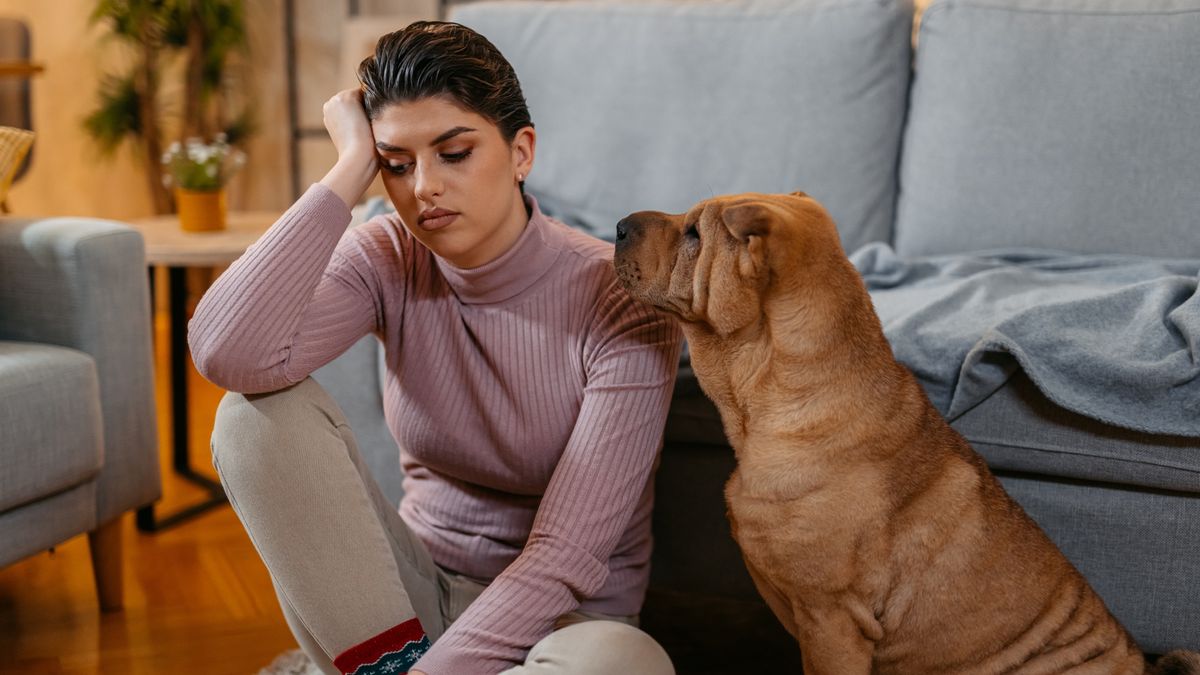 Woman sitting on floor of living room with dog beside her