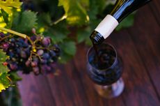 Pouring a glass of wine with grapes in background