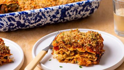 Slice of lasagne on a white plate with a blue and white dish in the background