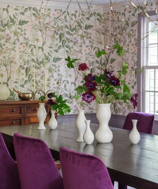 dining room with floral wallpaper, dark wood table, purple dining chairs, white vases, sideboard lilac painted woodwork, flowers