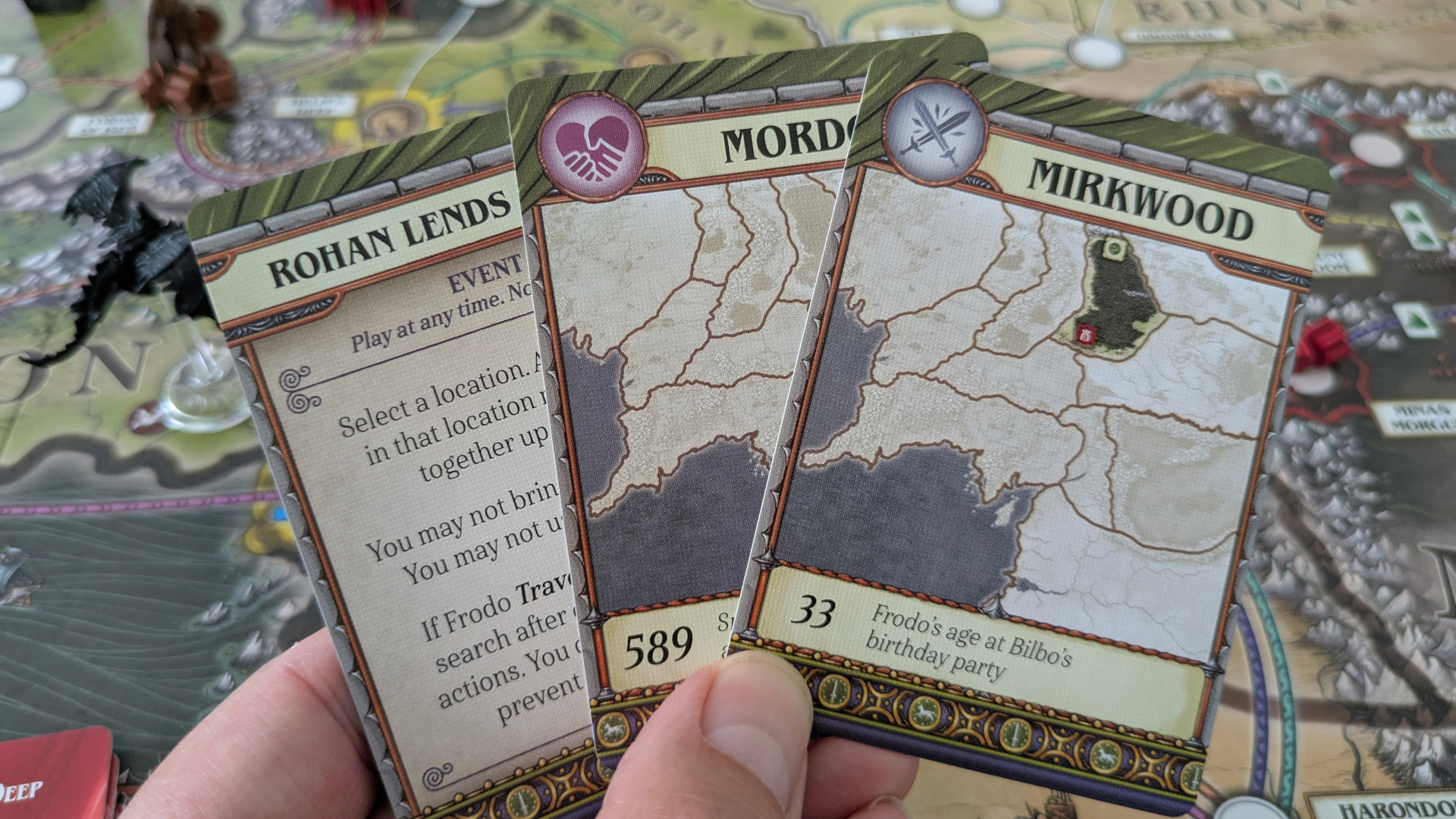A hand holds up three cards from Fate of the Fellowship in front of the board