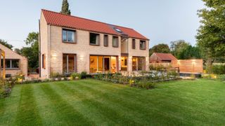 large modern light stone clad two storey home with red tiled roof and large lawned gardens