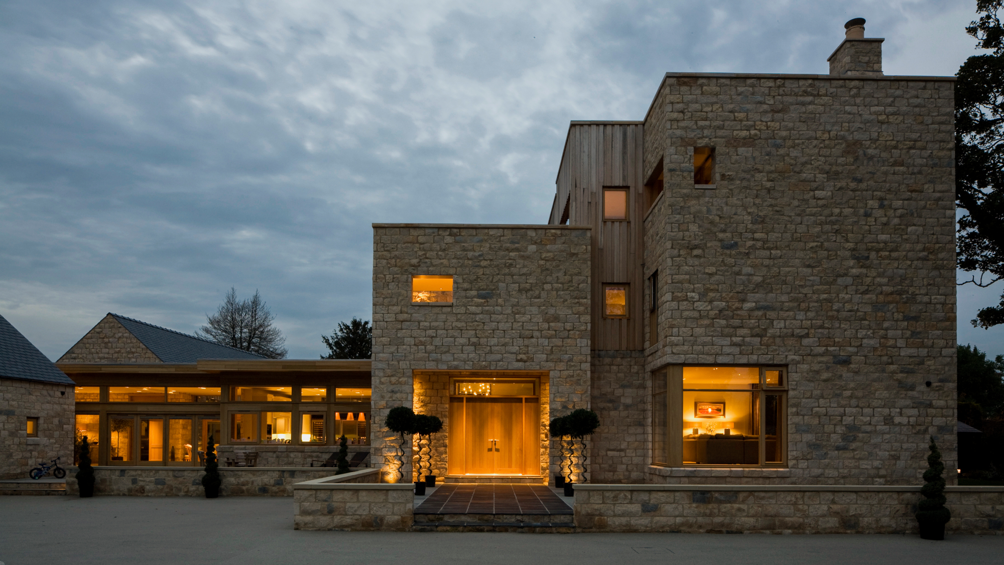 exterior of large brick and timber clad modern home showing home lit up at night from the inside
