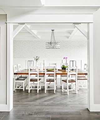 A dining room wall idea with white and grey wallpaper, white painted chairs and white beamed ceilings