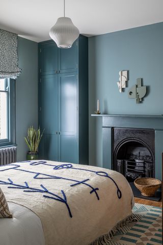 blue bedroom with blue wardrobe, throw blanket with blue stitched detail, original fireplace with sculptural art hanging above