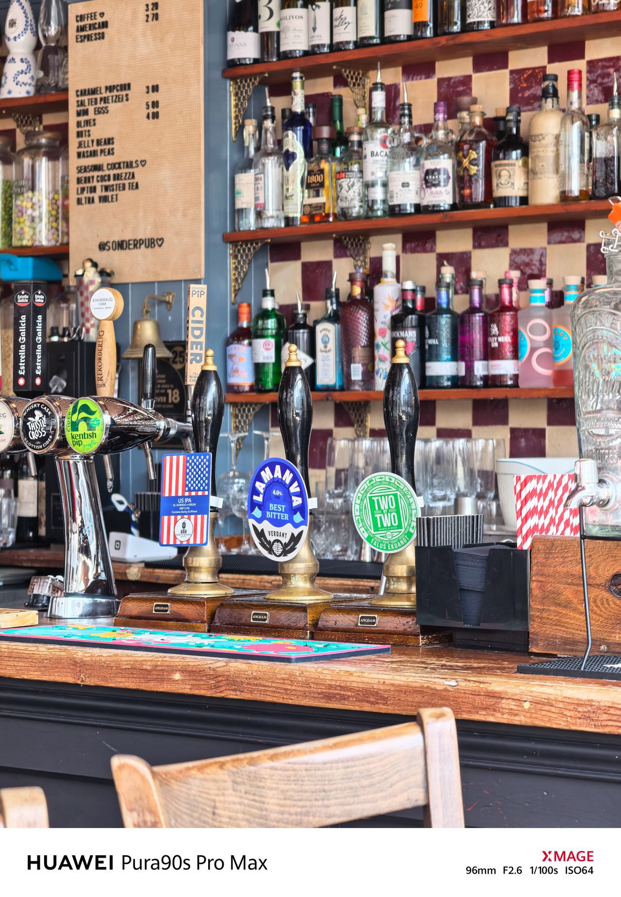 Colorful pub bar with beer taps, shelves of bottles, a menu board and wooden furnishings.