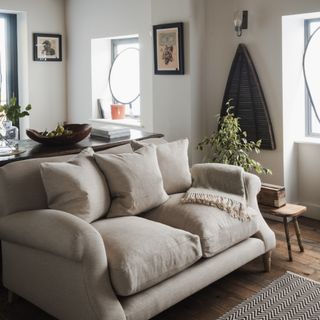 A living room with a beige 2-seater sofa and a matching throw, along with a wooden side and console tables with a wooden bowl of pears atop