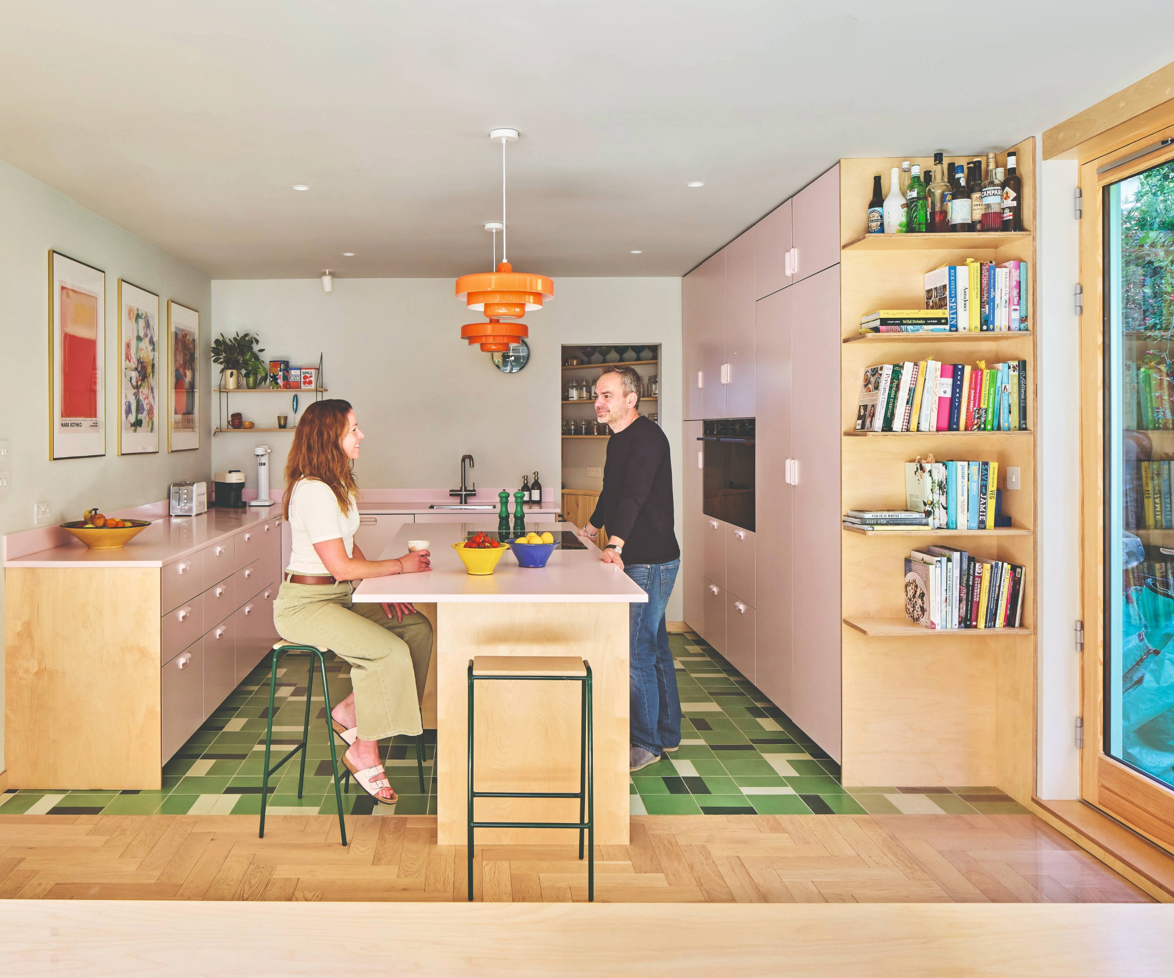 Homeowners sitting at the breakfast bar in the pink, orange and green kitchen