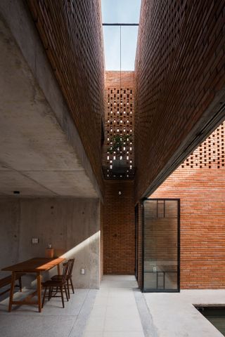 A courtyard with perforated brick and concrete flooring. On the left is a dark brown table and matching chairs