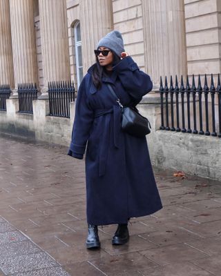 Woman wearing navy coat, black bag, gray beanie, and black zippered chunky Chelsea boots.