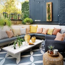 smart outdoor entertainment patio area with patterned tiles, a corner bench covered with cushions festoon lighting coffee table and footstool